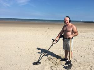 Man met metaaldetector op het strand