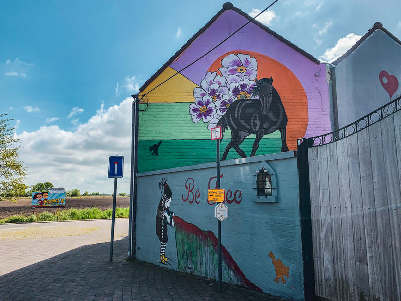 Kunstgevel van Annie Vanhee: meisje met pot verf en daarboven een paard tegen een kleurrijke achtergrond